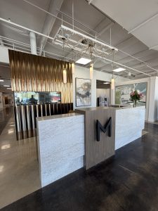Custom walnut and quartz waterfall-edge reception desk with backlit “M” logo at Montgomery's Furniture Gallery in Sioux Falls, SD.